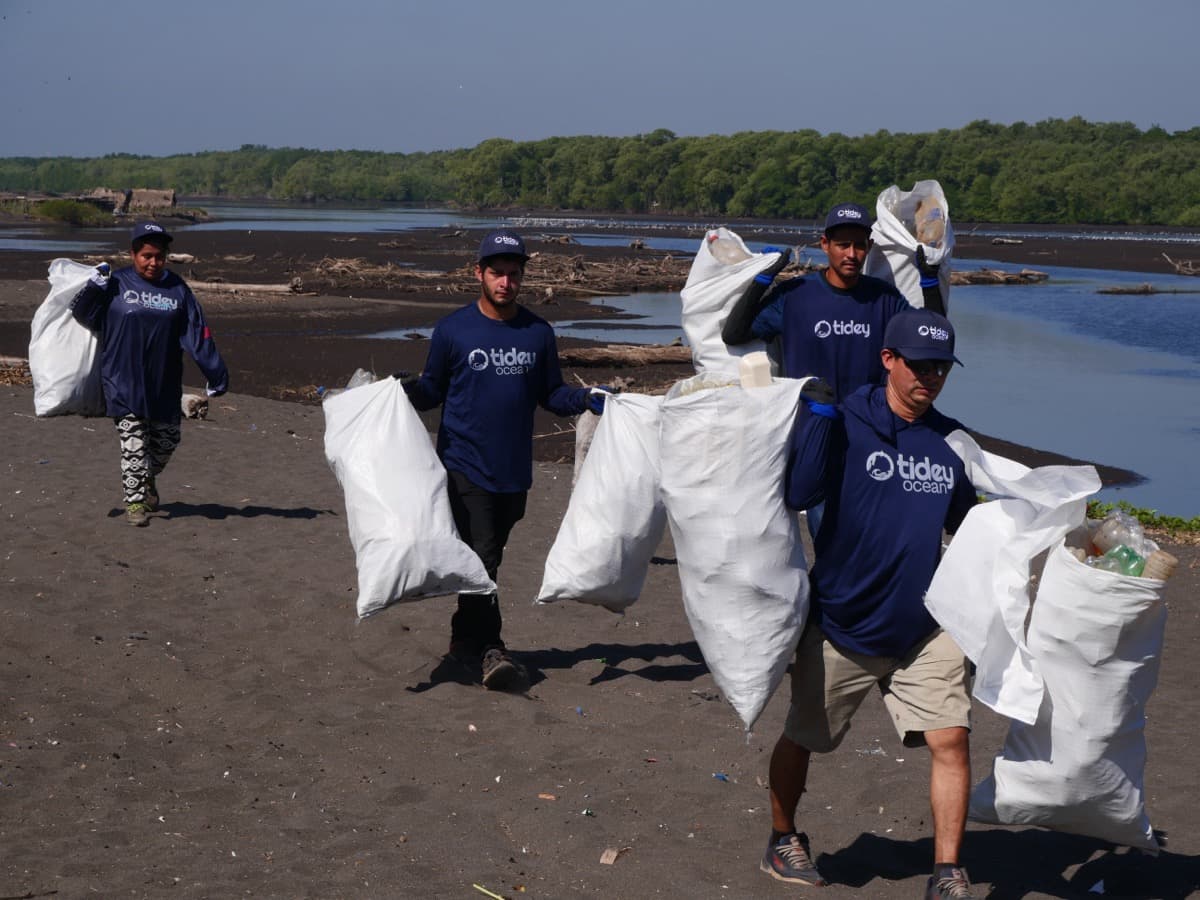 Tidey Ocean team carrying collected plastic bags on the beach